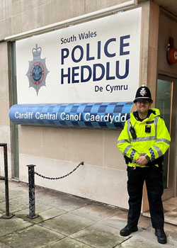 Police officer on right stands next to South Wales Police/Heddlu sign