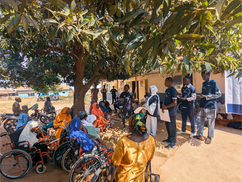 A group of volunteers teaching Disabled members of the community about AMR under a tree.
