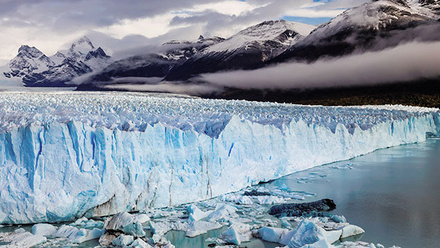 Blue glacier in the water with grey mountains in the background