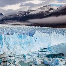 Blue glacier in the water with grey mountains in the background