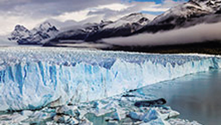 Blue glacier in the water with grey mountains in the background
