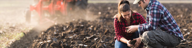 Farmers examing dirt while tractor is plowing field