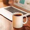 Cup of coffee in the front, blurred laptop in the background