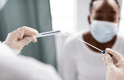 Doctor holding Covid swab with masked patient in the background